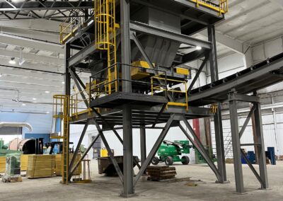 An industrial facility interior featuring large metal structures with yellow railings and machinery on the floor in the background.